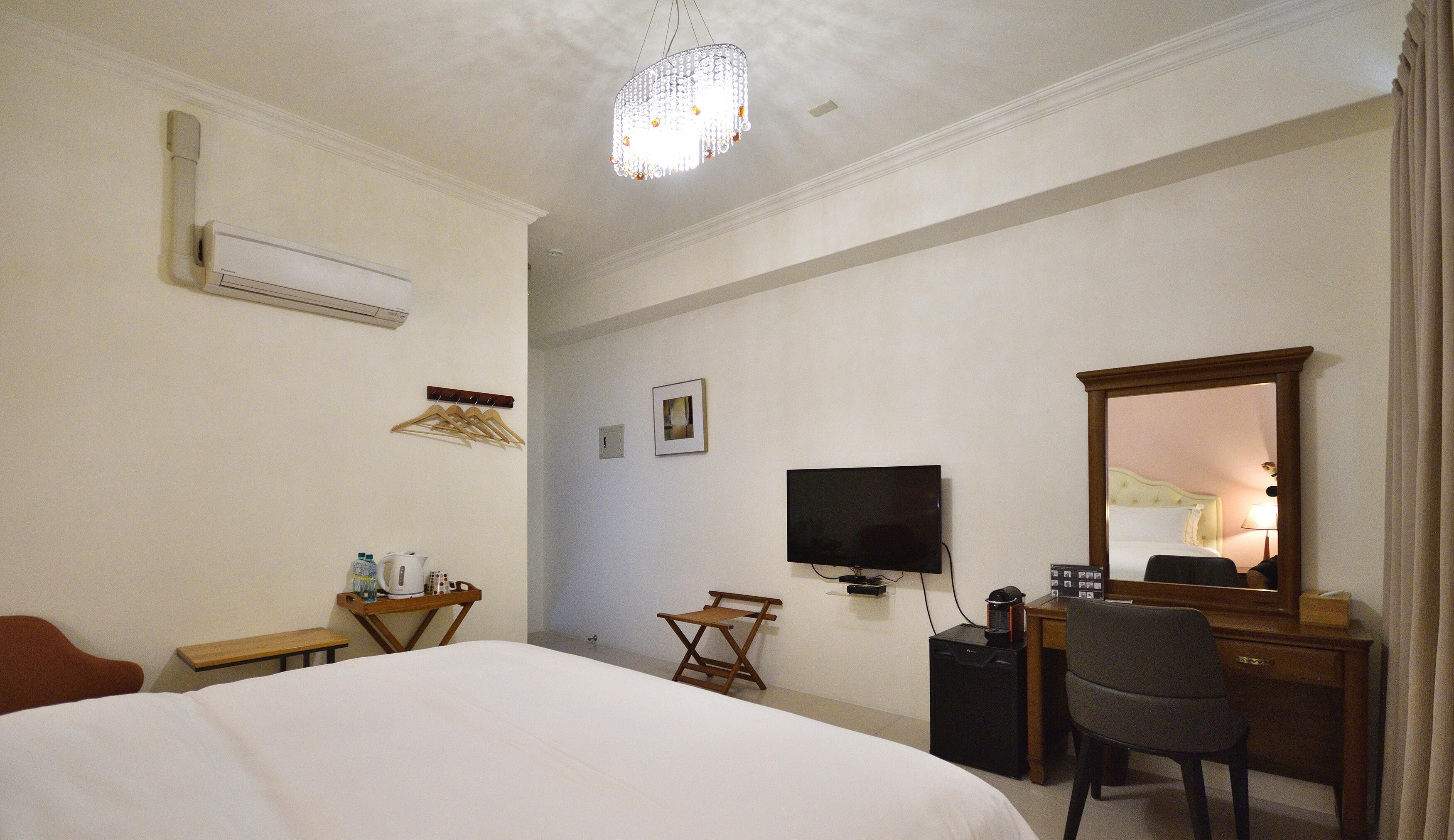 A hotel room with a large bed, a desk with a chair, a television, and a mirror.