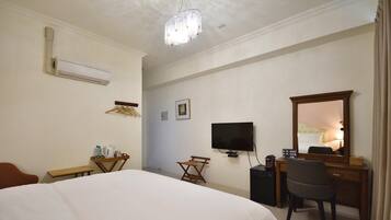 A hotel room with a large bed, a desk with a chair, a television, and a mirror.