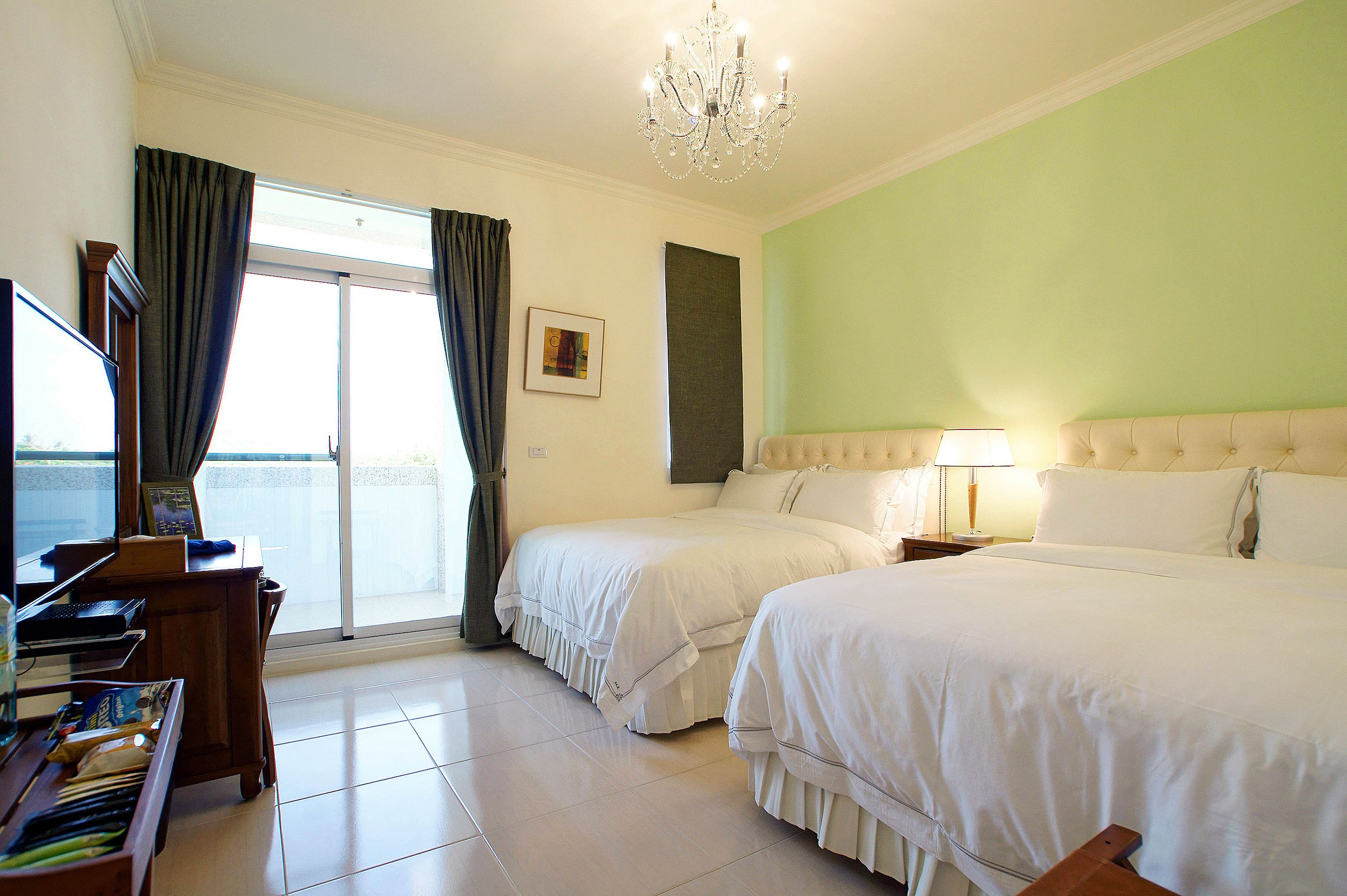 A hotel room with two beds, a piano, a chandelier, and a view of the sea through a large window.