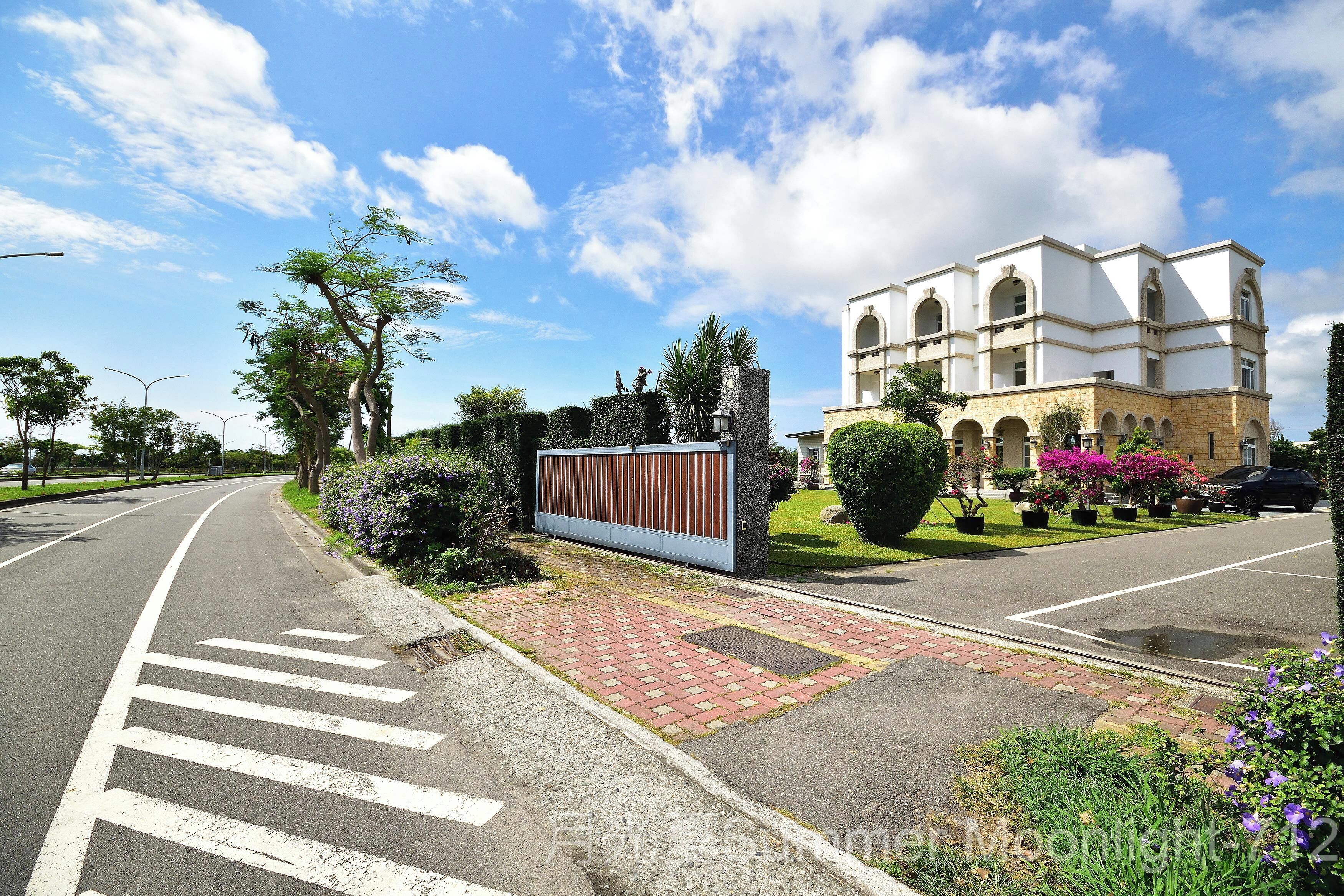 A road with a pedestrian crossing, a gated entrance, and a building with arched windows and a bell tower.