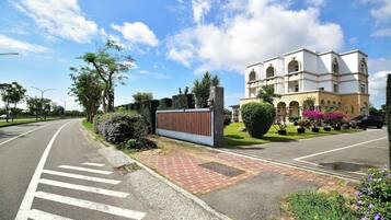 A road with a pedestrian crossing, a gated entrance, and a building with arched windows and a bell tower.