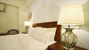 Una habitación de hotel con una cama bien hecha, un cabecero de madera, una mesita de noche con lámpara y una silla.