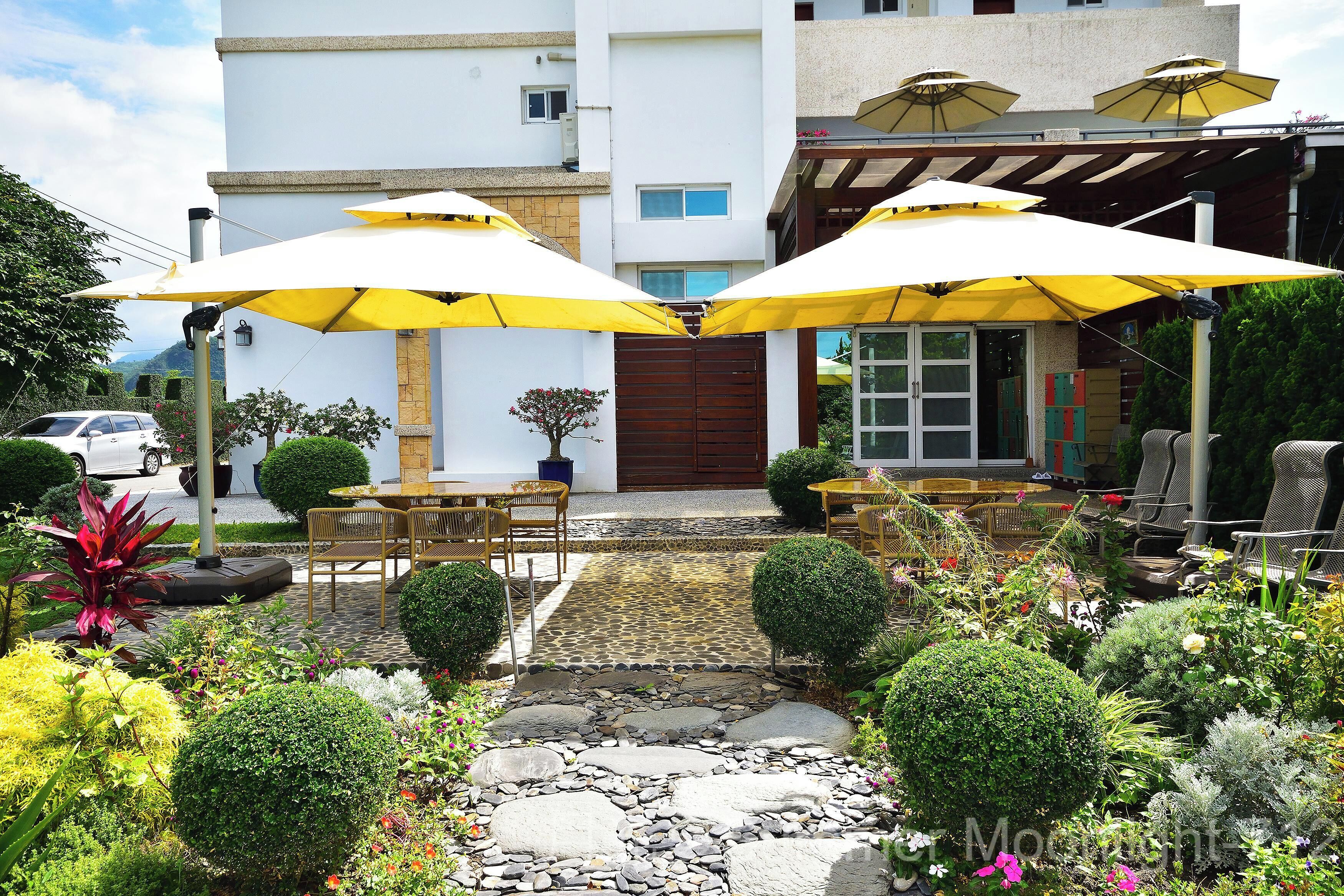 A patio area with outdoor seating, yellow umbrellas, and a stone pathway leading to a building entrance.