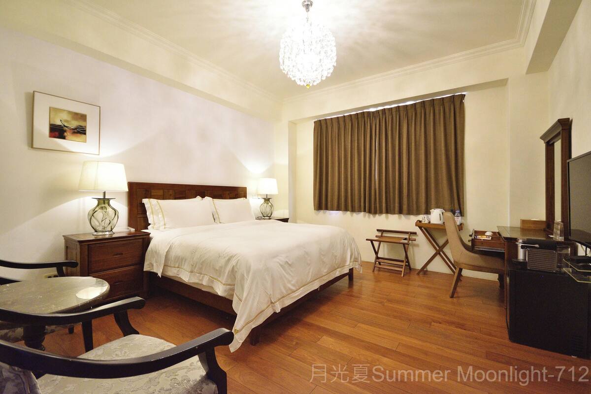 A hotel room with a bed, bedside tables, a desk, a chair, a television, and a window with curtains.