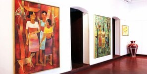 Uma galeria de arte com pinturas nas paredes e um vaso no chão.