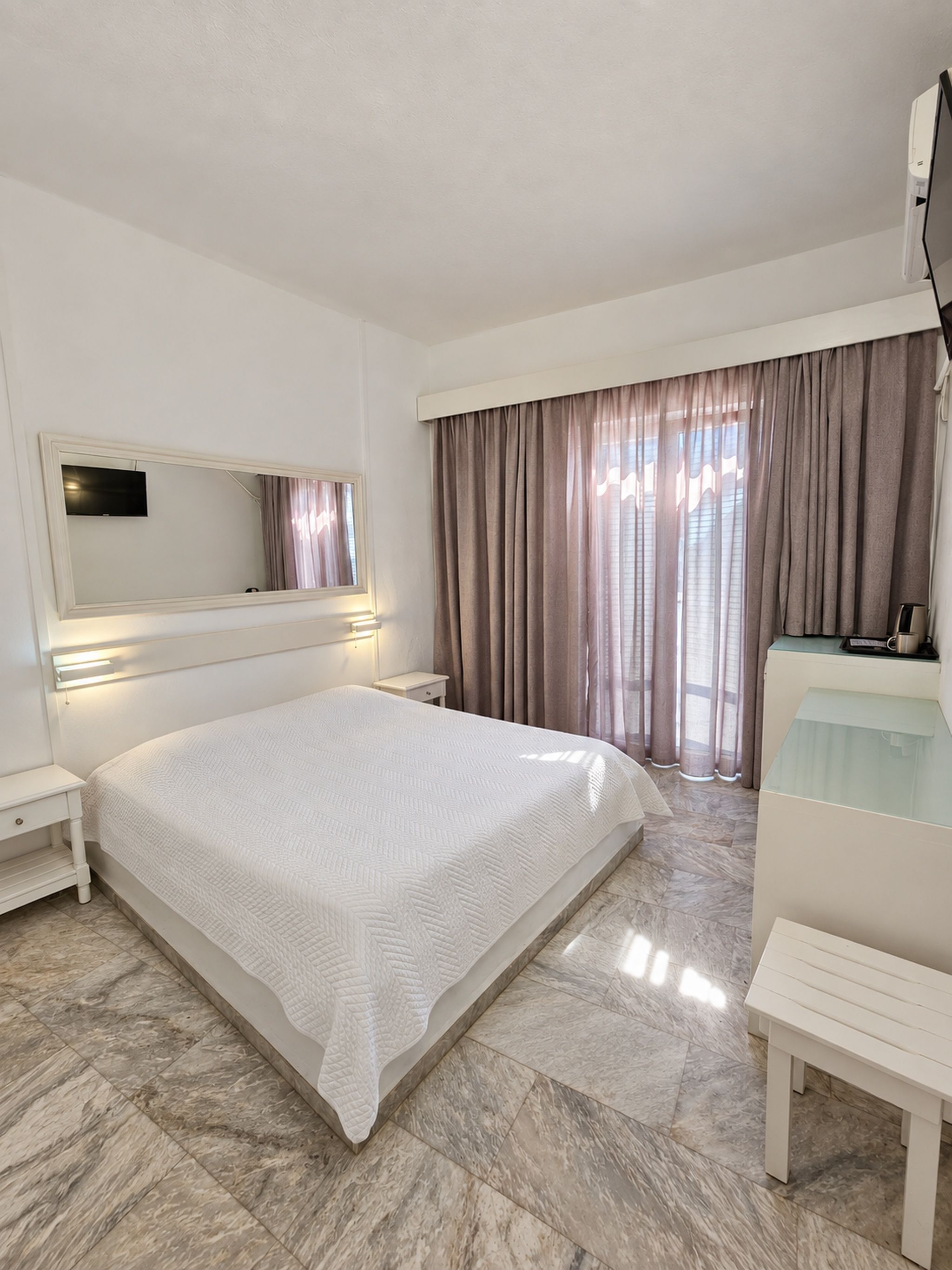 A hotel room with a large bed, a bedside table, a TV mounted on the wall, and a desk with a chair.