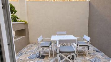 Un patio exterior con una mesa y sillas blancas, un suelo estampado y vistas a una colina.