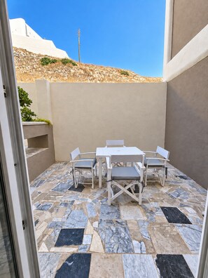 An outdoor patio with a white table and chairs, a patterned floor, and a view of a hill.
