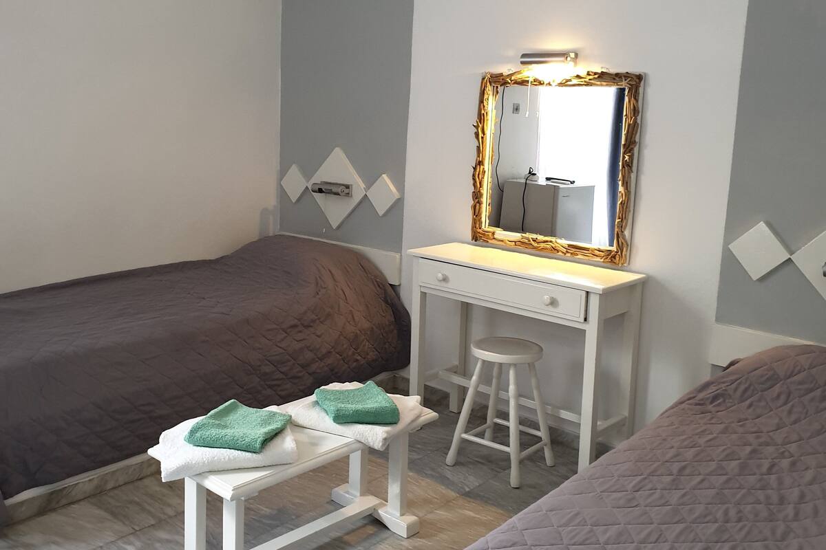 A bedroom with two beds, a white desk with a mirror, and a small stool.