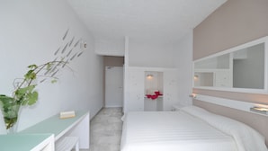 Une chambre à coucher comprenant un lit, un bureau, une chaise, un miroir et une porte donnant sur une salle de bain.