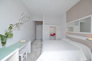 Un dormitorio con una cama, un escritorio, una silla, un espejo y una puerta que da al baño.