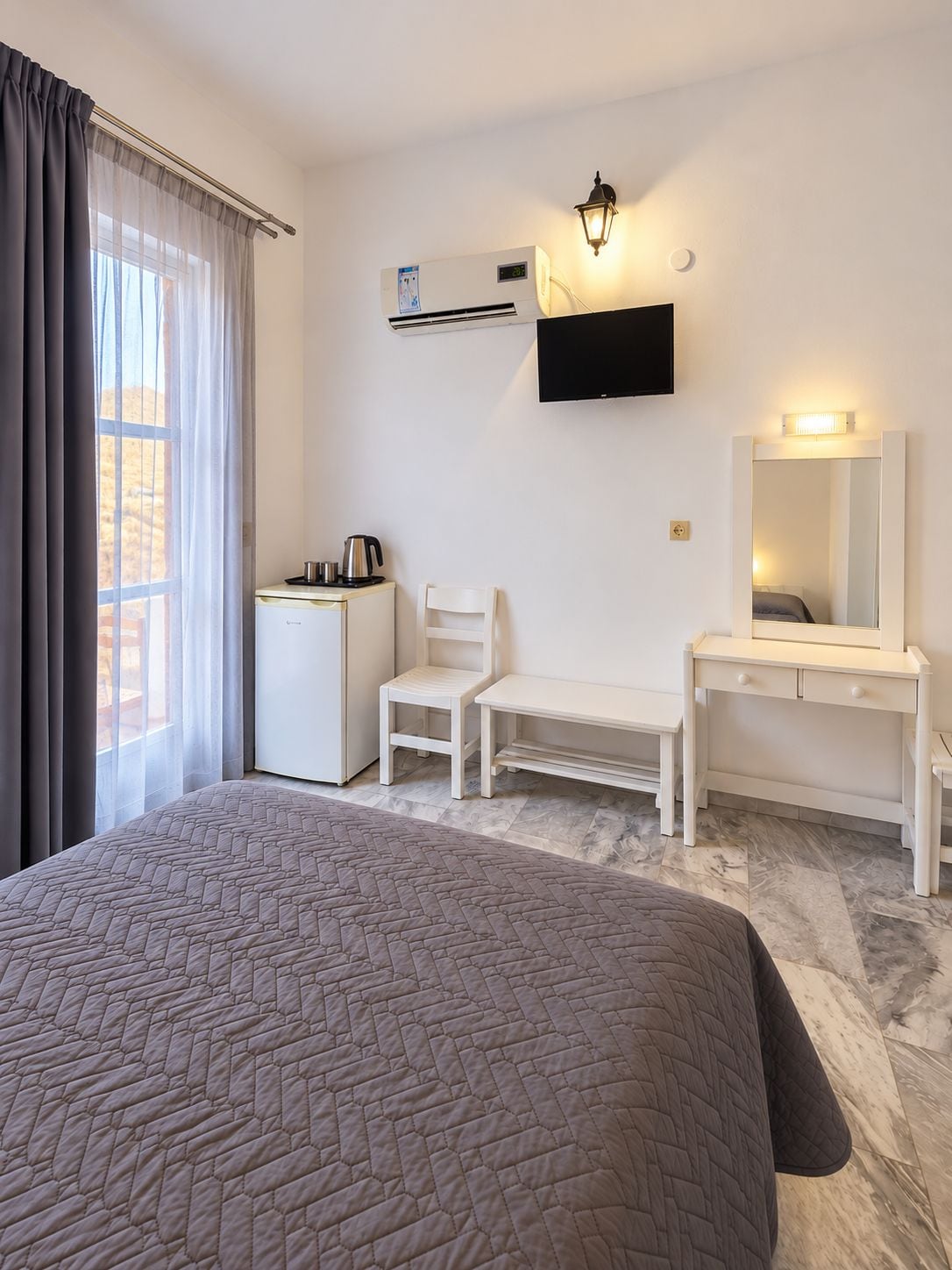 A hotel room with a bed, a desk, a chair, a flat-screen TV, and a wall-mounted air conditioner.