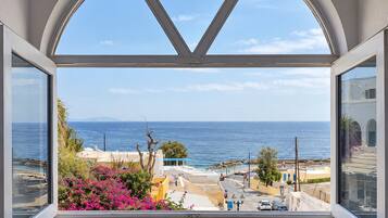 A view from a window with a white frame, overlooking a coastal town with buildings and the sea.