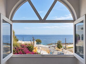 A view from a window with a white frame, overlooking a coastal town with buildings and the sea.