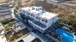 A multi-story building with balconies, a swimming pool, and a street view. - Porto Castello (Santorini)