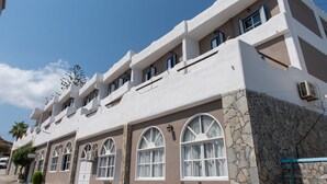 A multi-story building with a stone facade, arched windows, and balconies. - Porto Castello (Santorini)