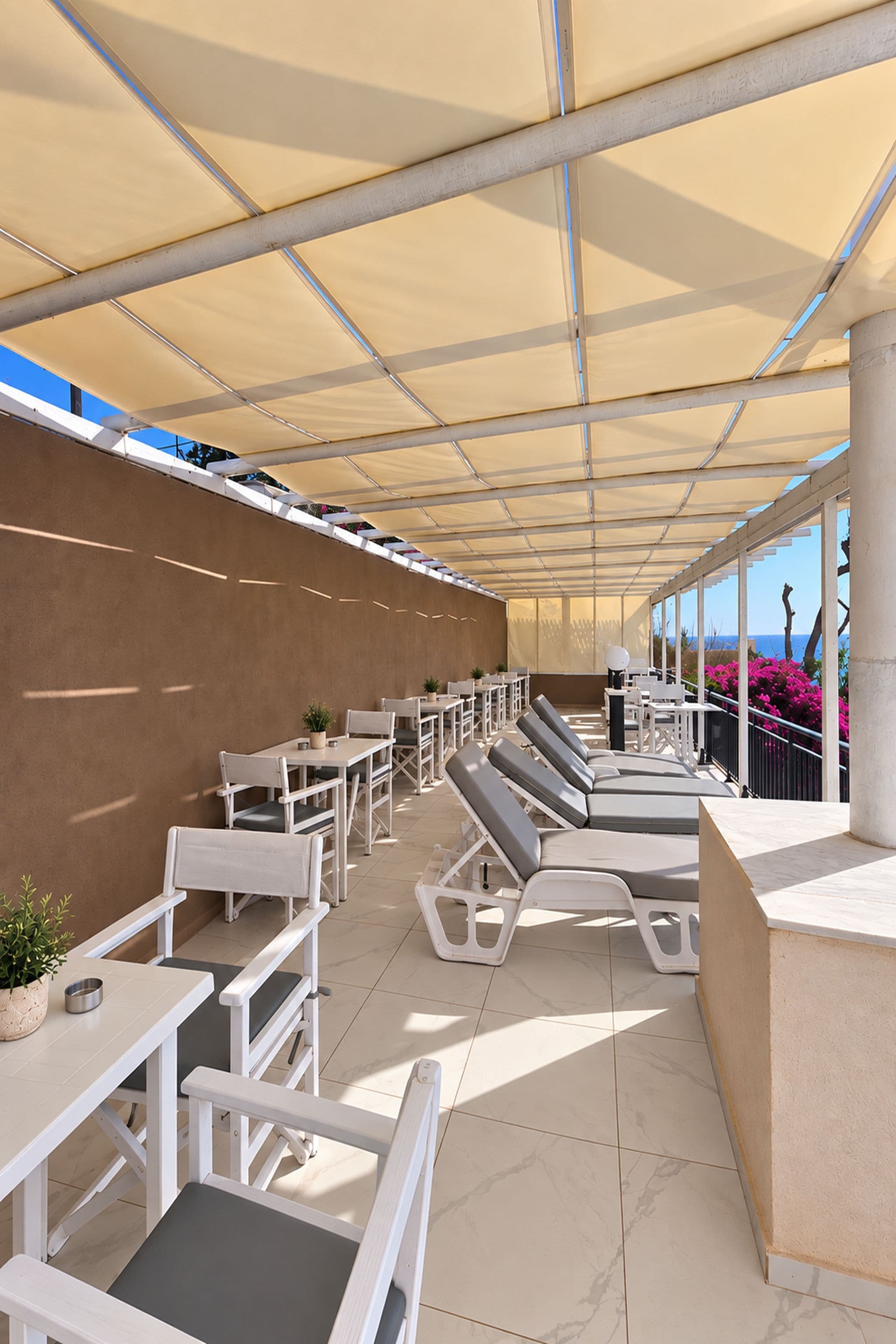 An outdoor seating area with tables and chairs, a covered walkway, and a view of the sea.