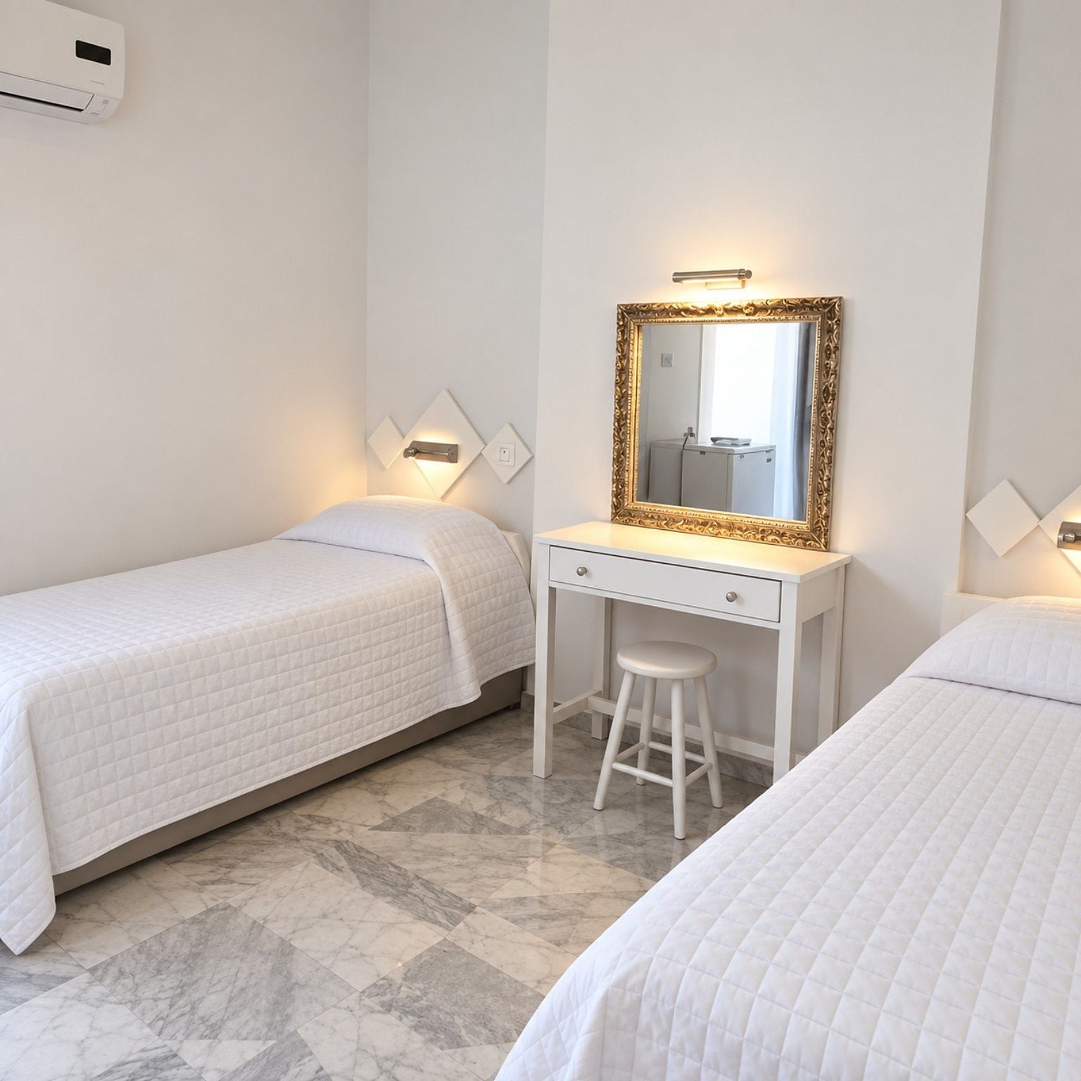 A hotel room with two single beds, a white desk with a mirror, and a wall-mounted air conditioner.