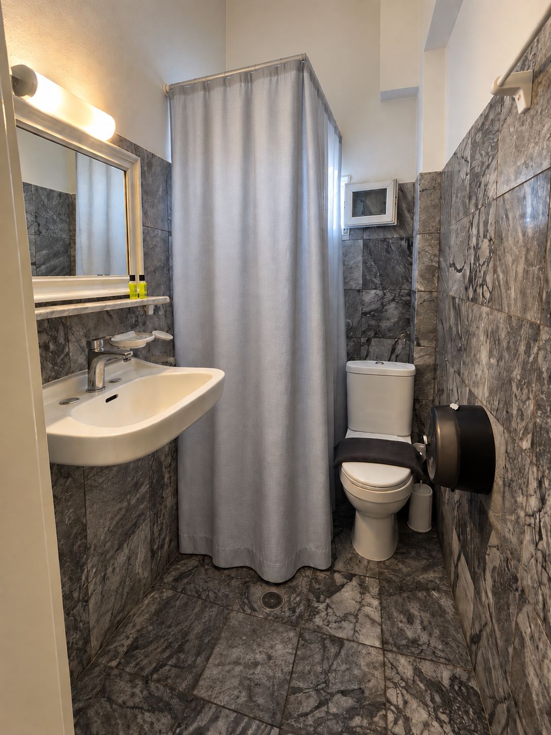 A bathroom with a shower curtain, a sink, a toilet, and a trash can.