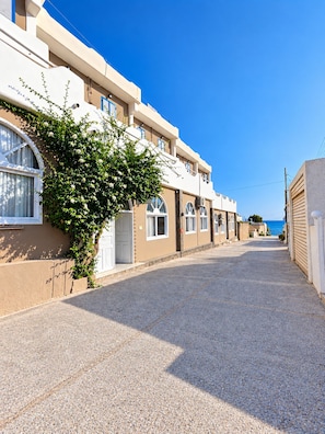 Una calle residencial con casas, cielo despejado y vista al mar en la distancia.