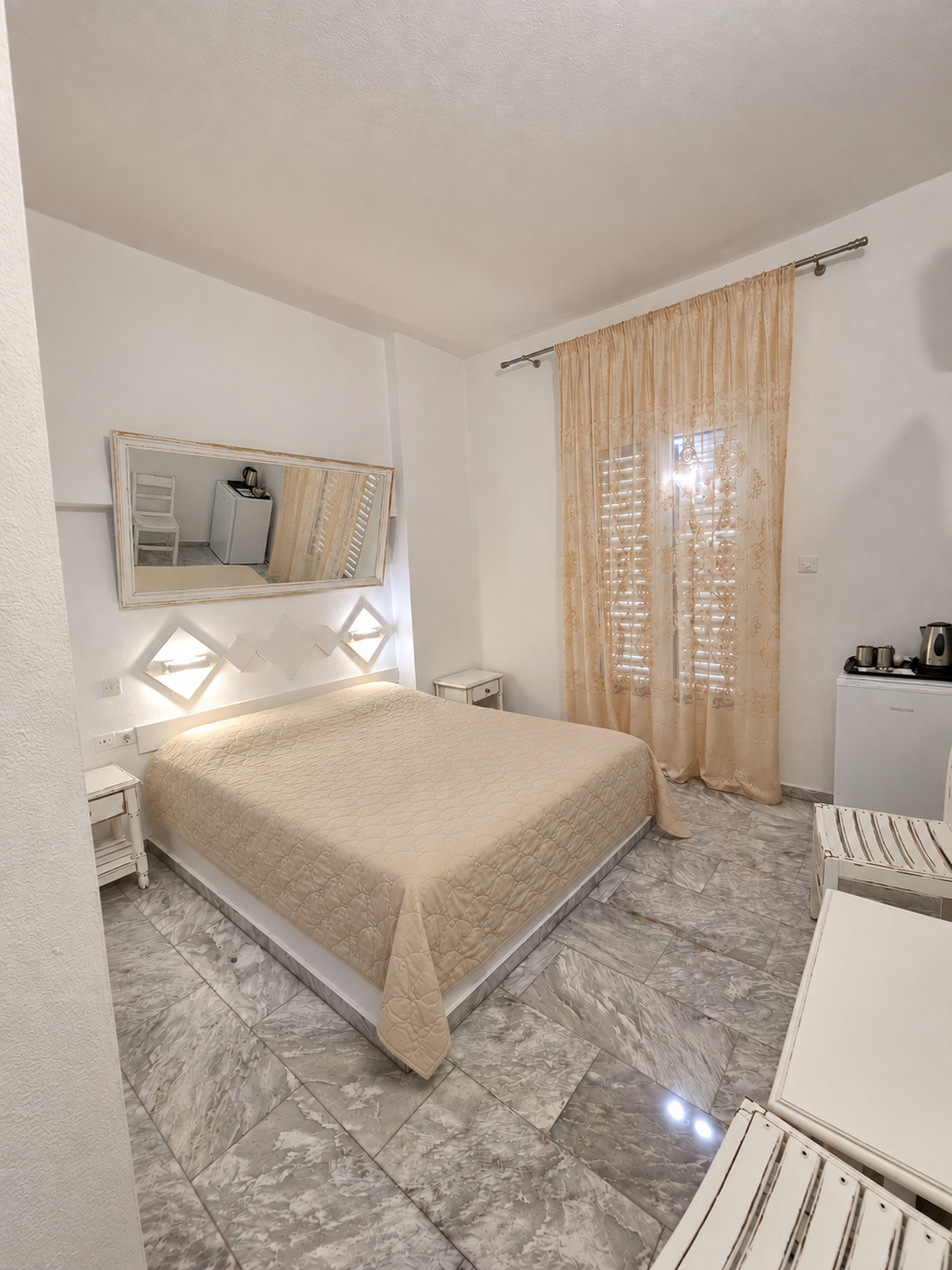 A bedroom with a bed, a bedside table, a mirror, a window with curtains, and a radiator.