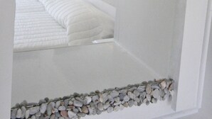 A bedroom with a bed, a mirror, and a wall-mounted light fixture. - Porto Castello (Santorini)