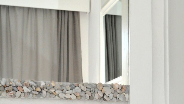 A white dresser with a decorative arrangement of pebbles and shells. - Porto Castello (Santorini)