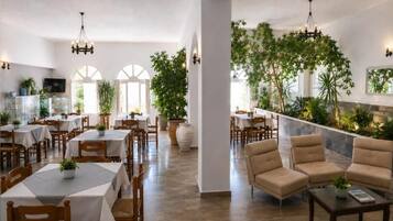 Ein Restaurant mit mehreren Tischen und Stühlen, einer Bar mit Theke sowie einer Sitzecke mit Sofas und einem Couchtisch.