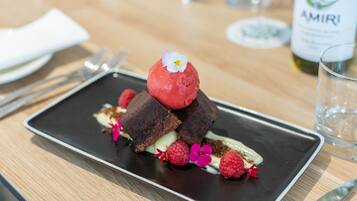 Un plato de postre con un pastel de chocolate, una bola de helado rojo, frambuesas y una flor sobre un plato rectangular.