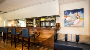 Un espace bar doté d’un comptoir en bois, de tabourets de bar et d’un coin salon avec un canapé et des coussins.