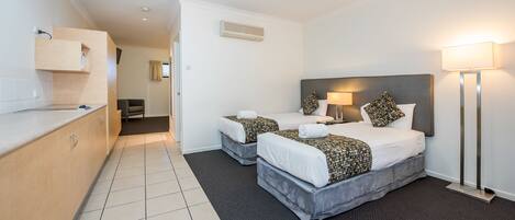 A hotel room with two beds, a desk, a chair, and a lamp.