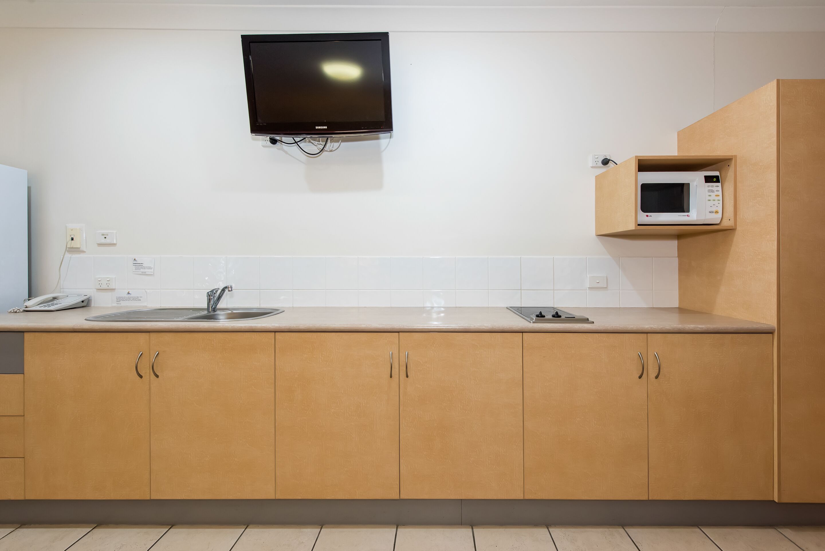 Een moderne keuken met houten kastjes, een ingebouwde magnetron, een flatscreen televisie en een gootsteen.