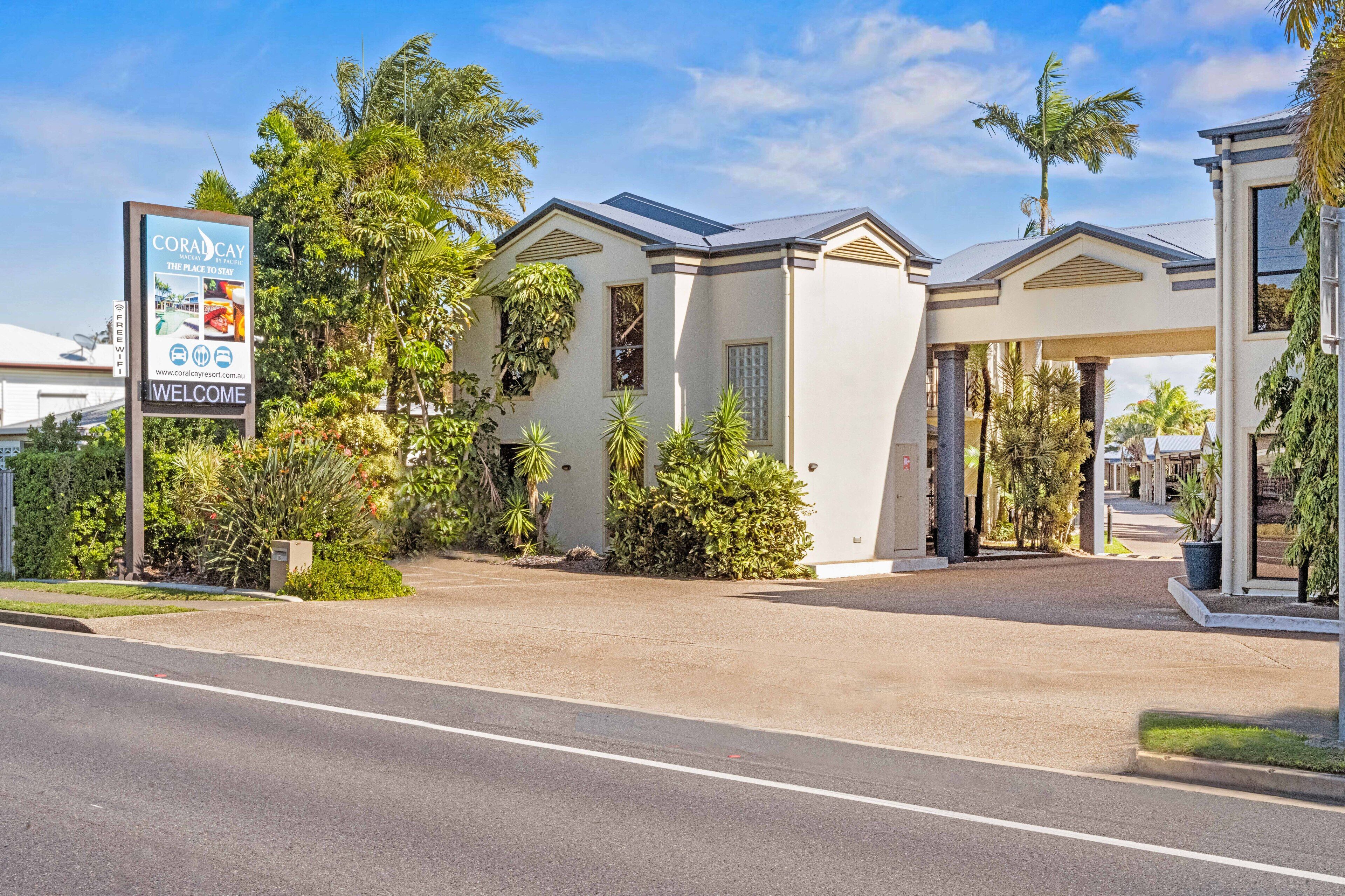 A modern hotel with a welcoming sign, a covered entrance, and lush landscaping.