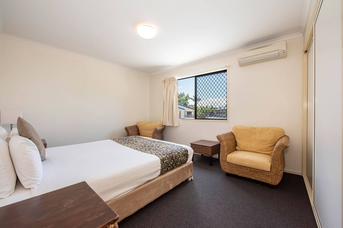 A hotel room with a large bed, a small table, a chair, and a window with a view.