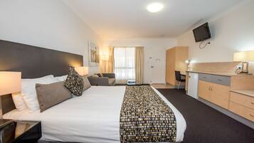 A hotel room with a large bed, a desk, a TV, and a kitchenette.