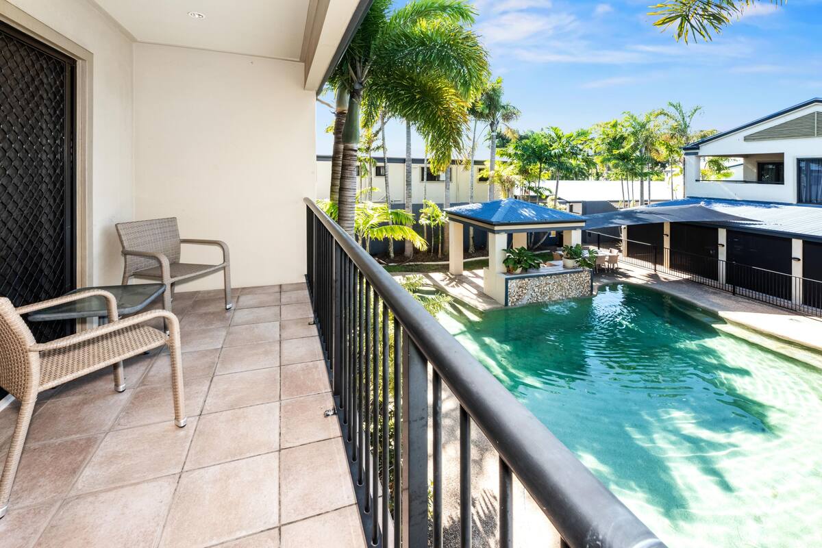 A balcony with a pool, wicker furniture, and a covered seating area.