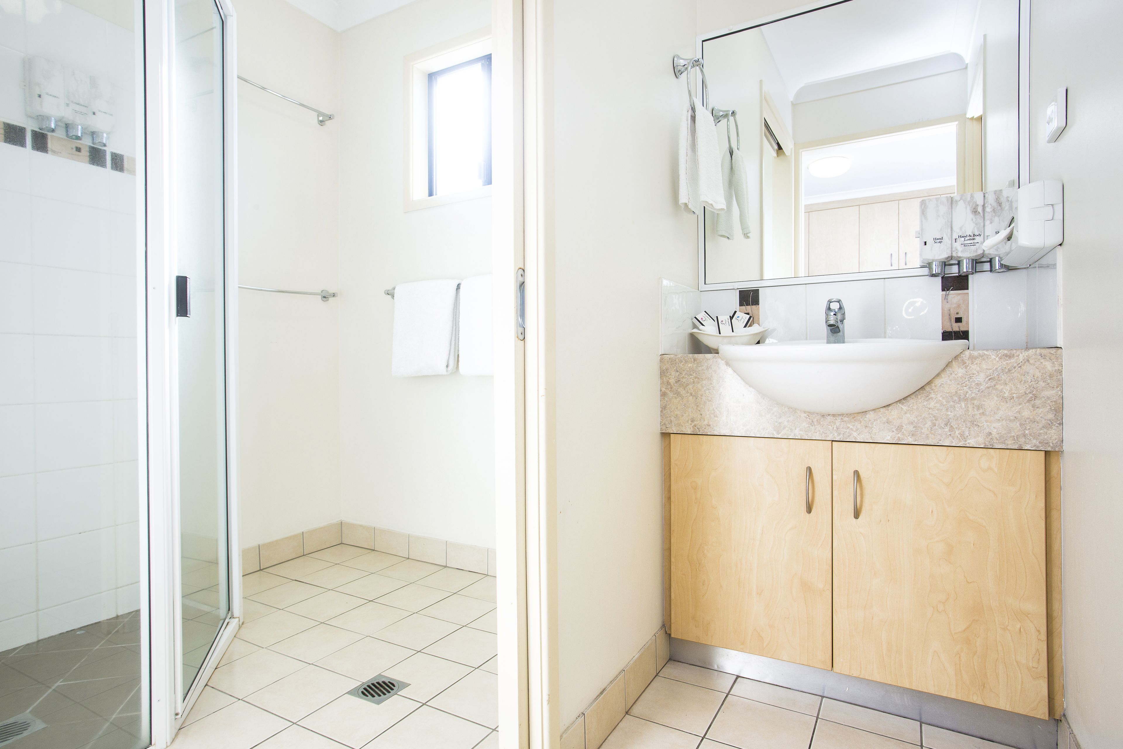 A modern bathroom with a glass shower enclosure, a sink with a marble countertop, and wooden cabinets.