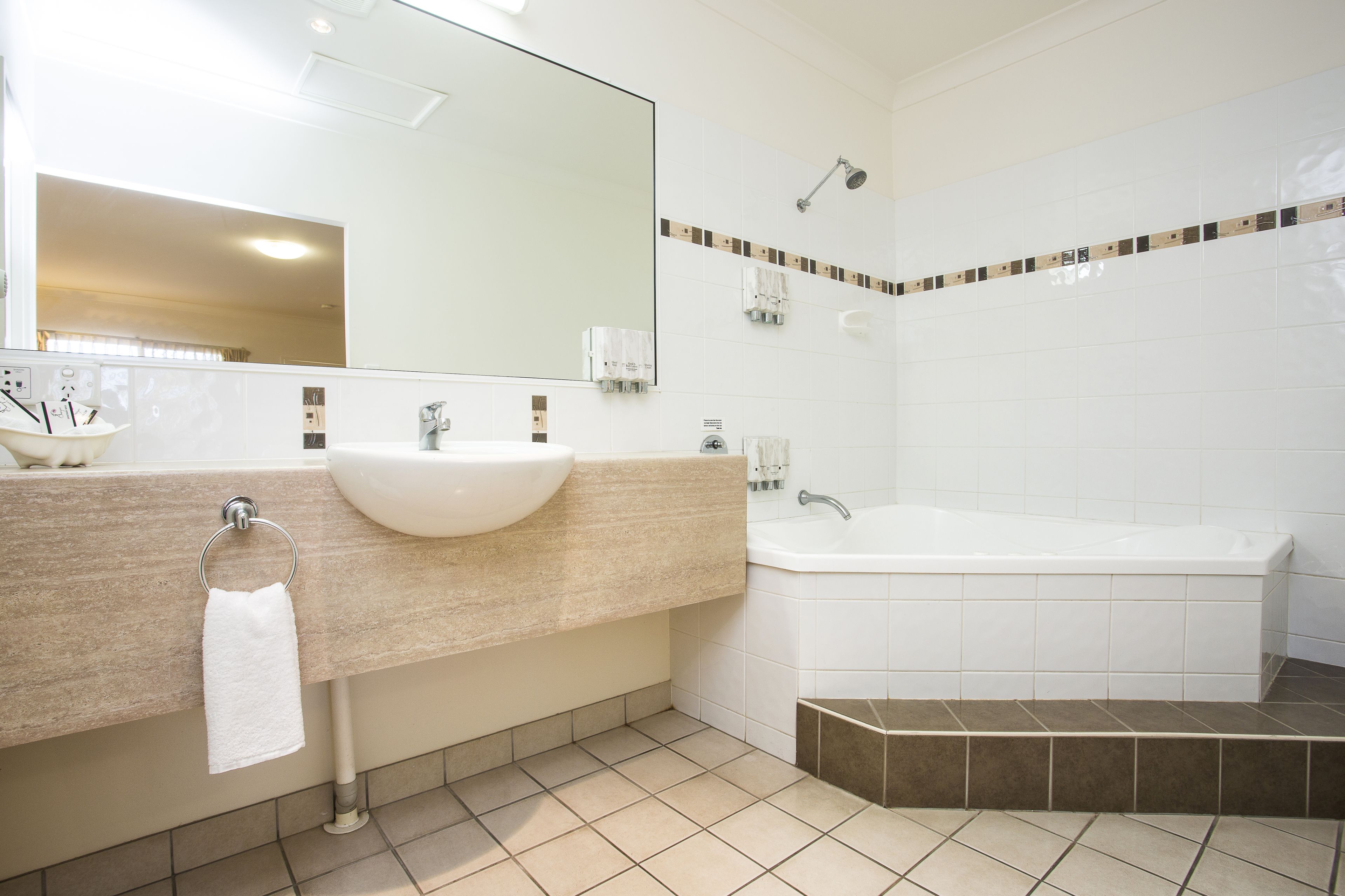 Un baño moderno con un tocador color beige, un lavamanos blanco, un espejo grande, una bañera y una ducha.