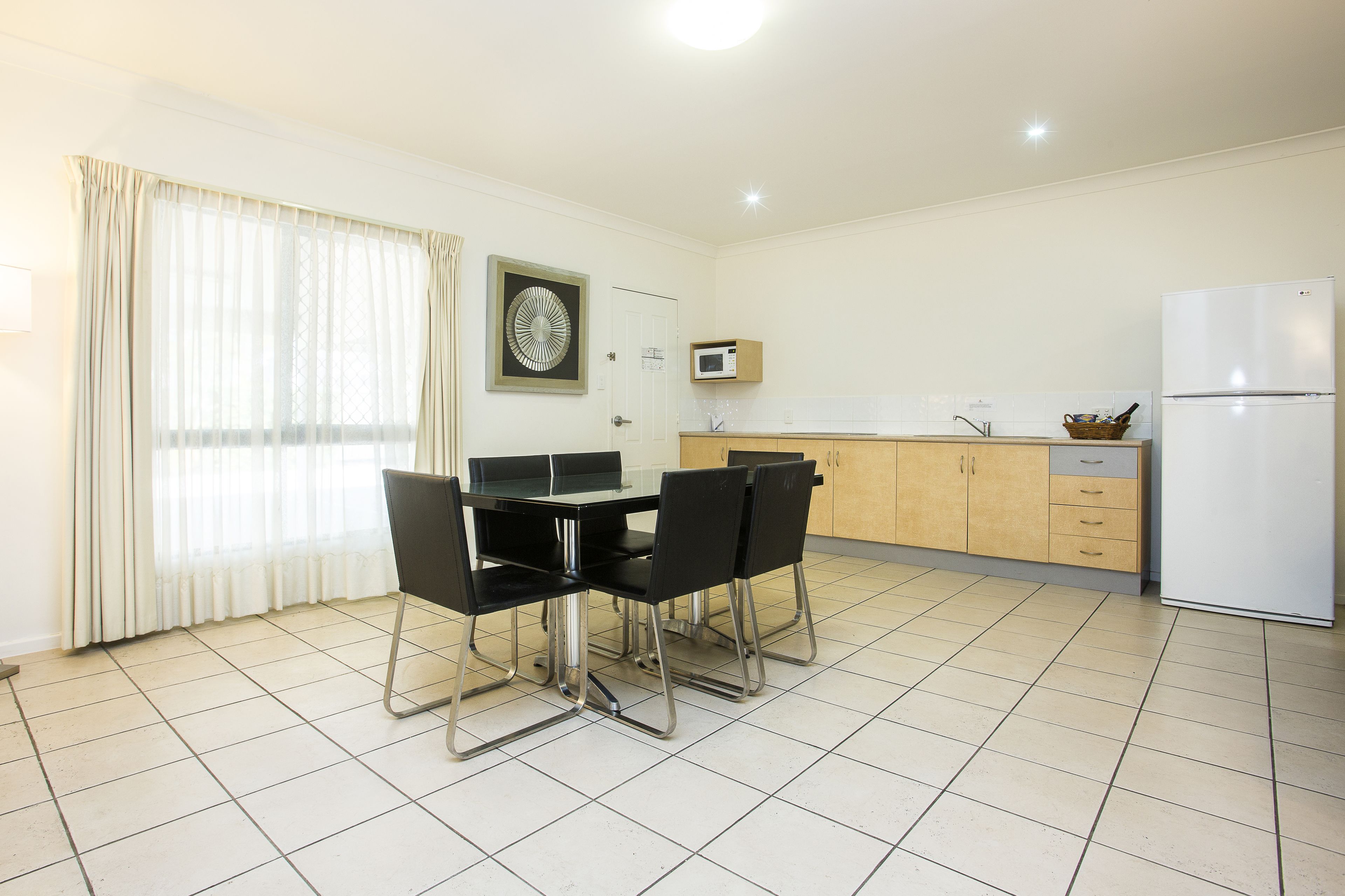 A modern kitchen with a dining table, chairs, a refrigerator, and a microwave.