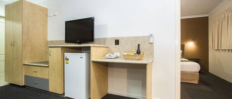 Habitación compacta con kitchenette, televisión de pantalla plana, refrigerador pequeño, escritorio con cesta y teléfono, y cama en la habitación contigua.