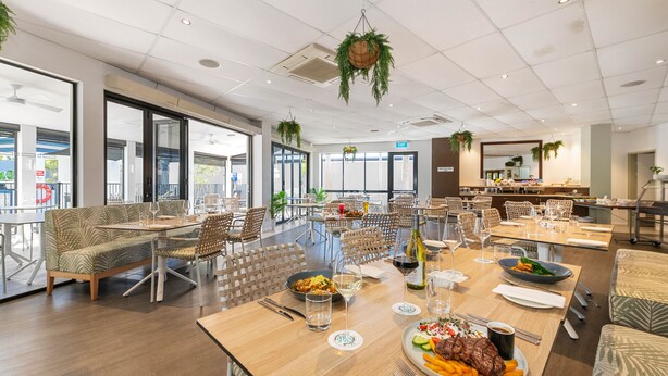Un vaste espace dédié à la salle à manger, avec de nombreuses tables et chaises, de grandes fenêtres et des plantes suspendues.