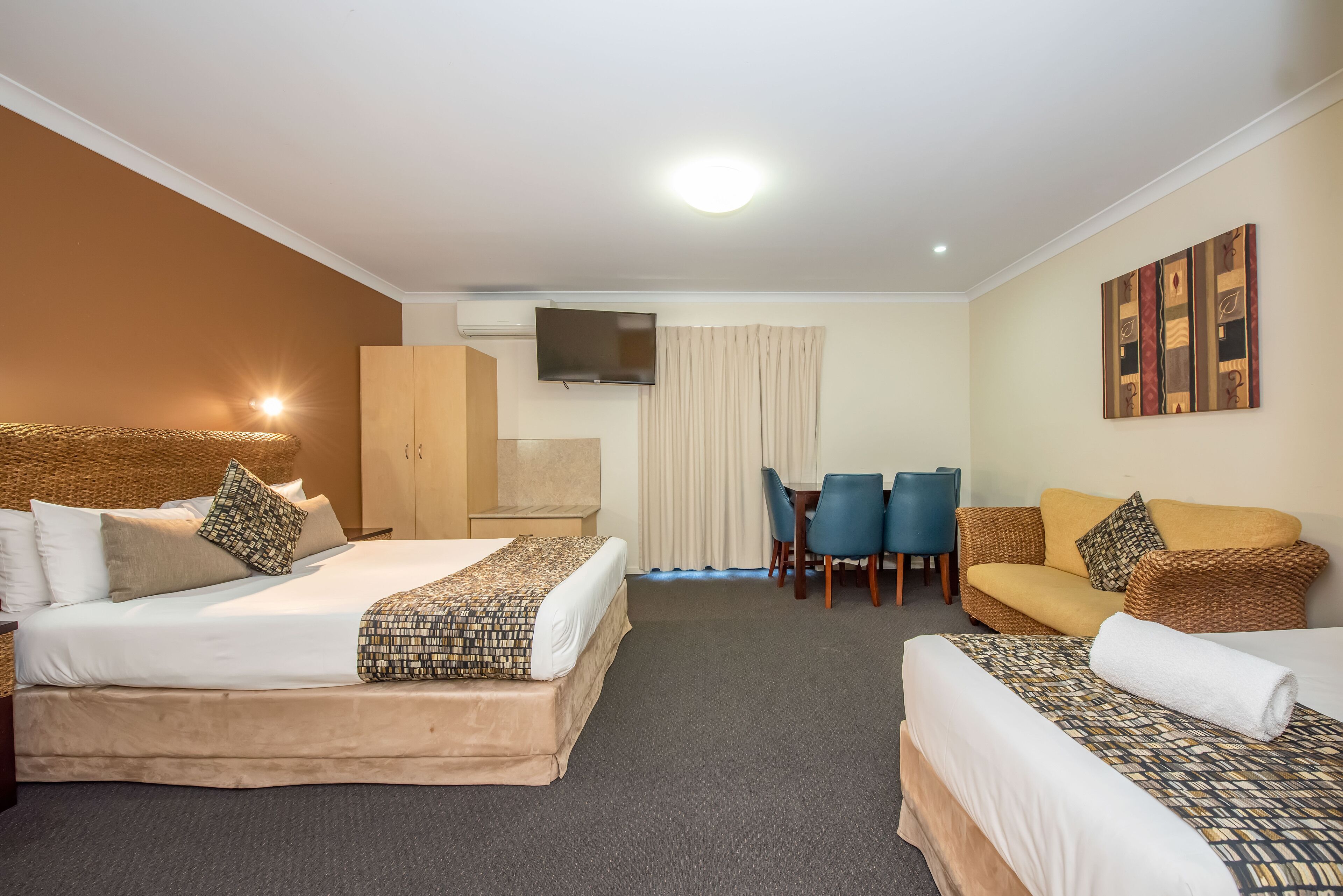 Quarto de hotel com duas camas, televisão, mesa de jantar com cadeiras e obras de arte nas paredes.