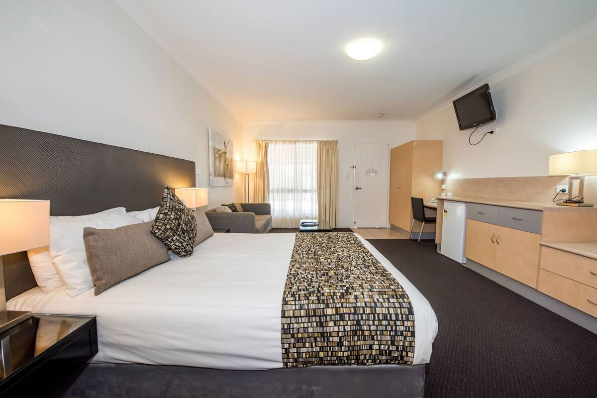 A hotel room with a large bed, a desk, a TV, and a window with curtains.