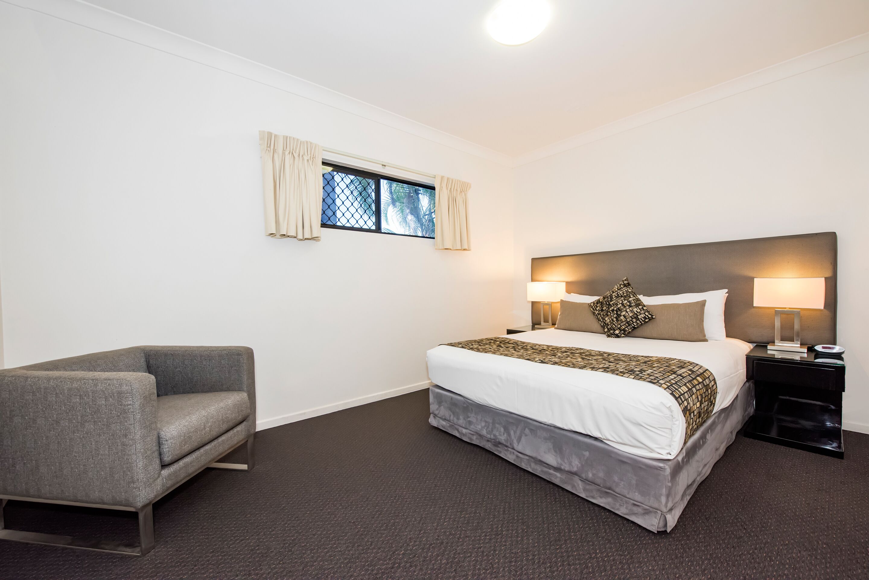 A hotel room with a bed, a chair, a nightstand, and a window with curtains.