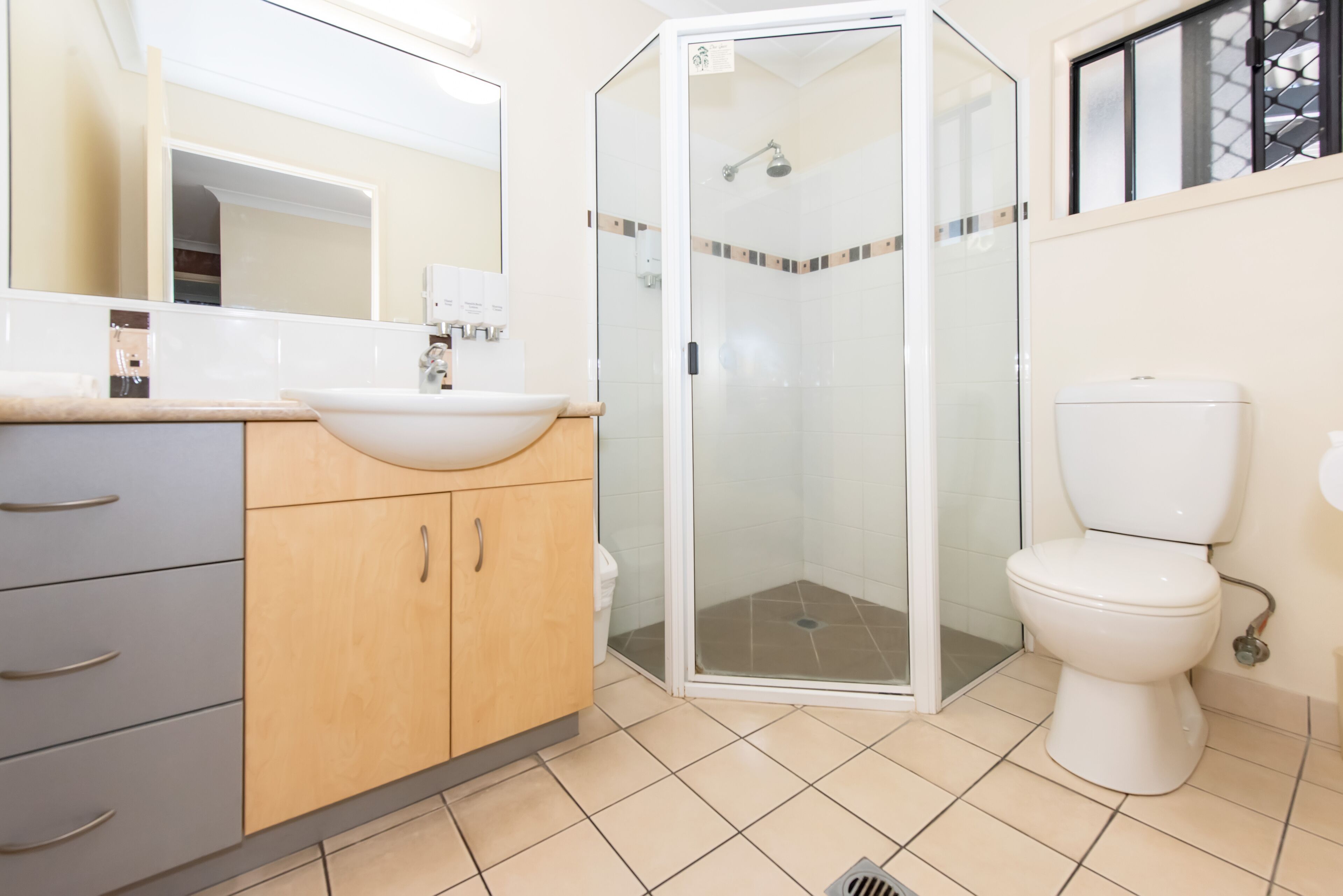 A modern bathroom with a glass-enclosed shower, a white toilet, and a sink with a beige countertop.