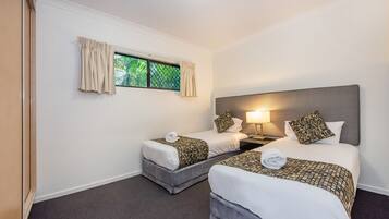 A hotel room with two beds, a window with curtains, a nightstand with a lamp, and a headboard.