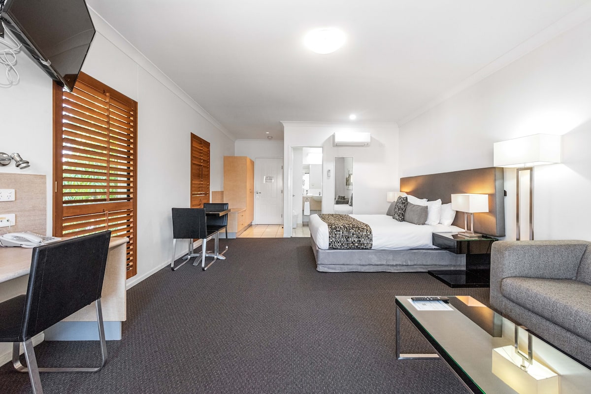 A hotel room with a bed, desk, chair, and a sofa.