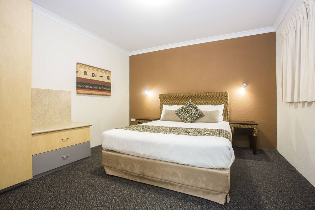 A hotel room with a large bed, a nightstand, a dresser, and a wall-mounted artwork.
