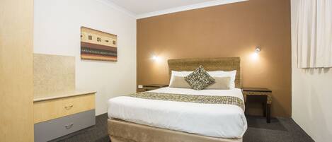 A hotel room with a large bed, a nightstand, a dresser, and a wall-mounted artwork.