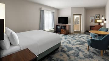 A hotel room with a large bed, a desk, a television, and a seating area with chairs.